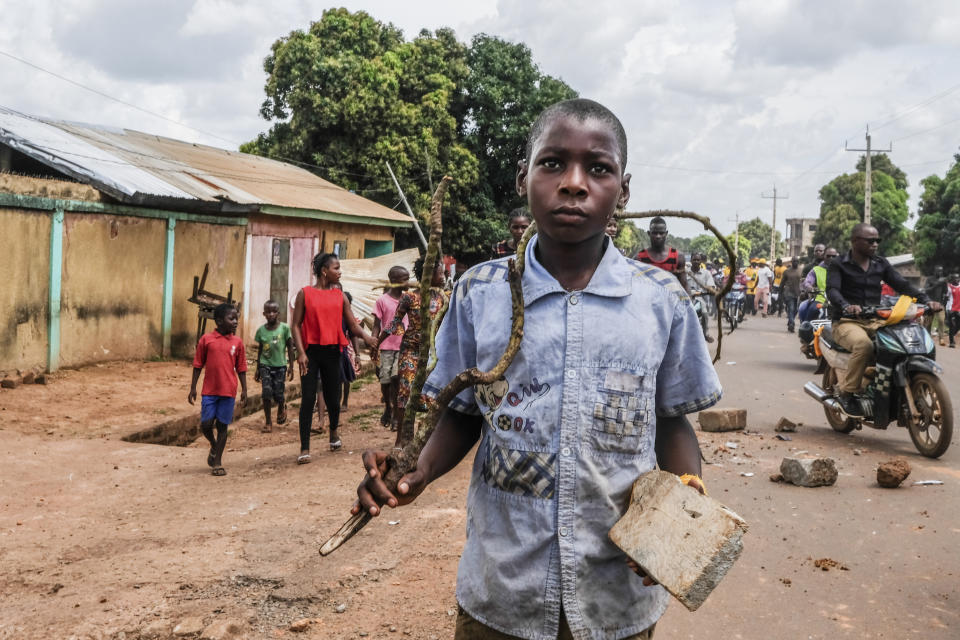 A child holds a stick and rock as supporters of the ruling Rally of the Guinean People (RPG) party demonstrate against the opposition Union of Democratic Forces of Guinea (UFDG) party and to block the visit of their leader, in the streets of Kankan, Guinea Sunday, Oct. 11, 2020. The stage is set for Oct. 18 presidential elections pitting incumbent President Alpha Conde, 82, who is bidding for a third term, against opposition leader Cellou Dalein Diallo, who was previously defeated by Conde in both the 2010 and 2015 elections. (AP Photo/Sadak Souici)