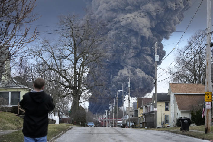 A man takes photos as a black plume rises over East Palestine, Ohio, as a result of a controlled detonation of a portion of the derailed Norfolk Southern trains Monday, Feb. 6, 2023. (AP Photo/Gene J. Puskar)