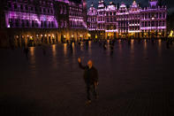 A passersby strolls and takes photographs on Grand Place during an autumn evening prior to the curfew in downtown Brussels, Friday, Oct. 23, 2020. In much of Europe, city squares and streets, be they wide, elegant boulevards like in Paris or cobblestoned alleys in Rome, serve as animated evening extensions of drawing rooms and living rooms. As Coronavirus restrictions once again put limitations on how we live and socialize, AP photographers across Europe delivered a snapshot of how Friday evening, the gateway to the weekend, looks and feels. (AP Photo/Francisco Seco)