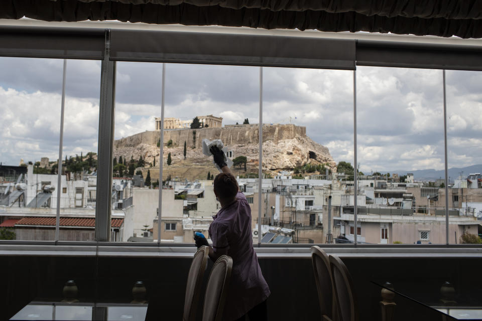 FILE - In this Monday, June 1, 2020 file photo, hotel worker Mailinda Kaci cleans the windows in a restaurant area at the Acropolian Spirit Hotel in central Athens with the ancient Acropolis in the background. The coronavirus pandemic is gathering strength again in Europe and, with winter coming, its restaurant industry is struggling. The spring lockdowns were already devastating for many, and now a new set restrictions is dealing a second blow. Some governments have ordered restaurants closed; others have imposed restrictions curtailing how they operate. (AP Photo/Petros Giannakouris, File)