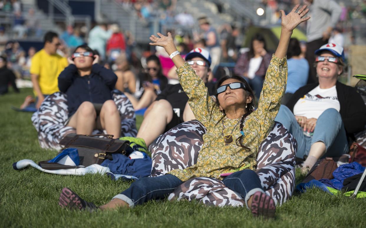  People wearing solar eclipse glasses sit in the grass to view the 2017 total solar eclipse over North America. 
