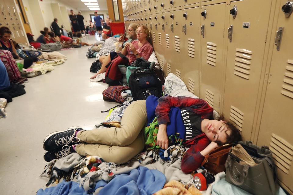 FILE - In this Oct. 10, 2018 file photo, Emily Hindle lies on the floor at an evacuation shelter set up at Rutherford High School, in advance of Hurricane Michael, in Panama City Beach, Fla. As each day brings the United States closer to peak severe weather season, Tornado Alley residents are facing a difficult question: Is it better to take on a twister outside a community shelter or to face the possibility of contracting the new coronavirus inside one? (AP Photo/Gerald Herbert, File)