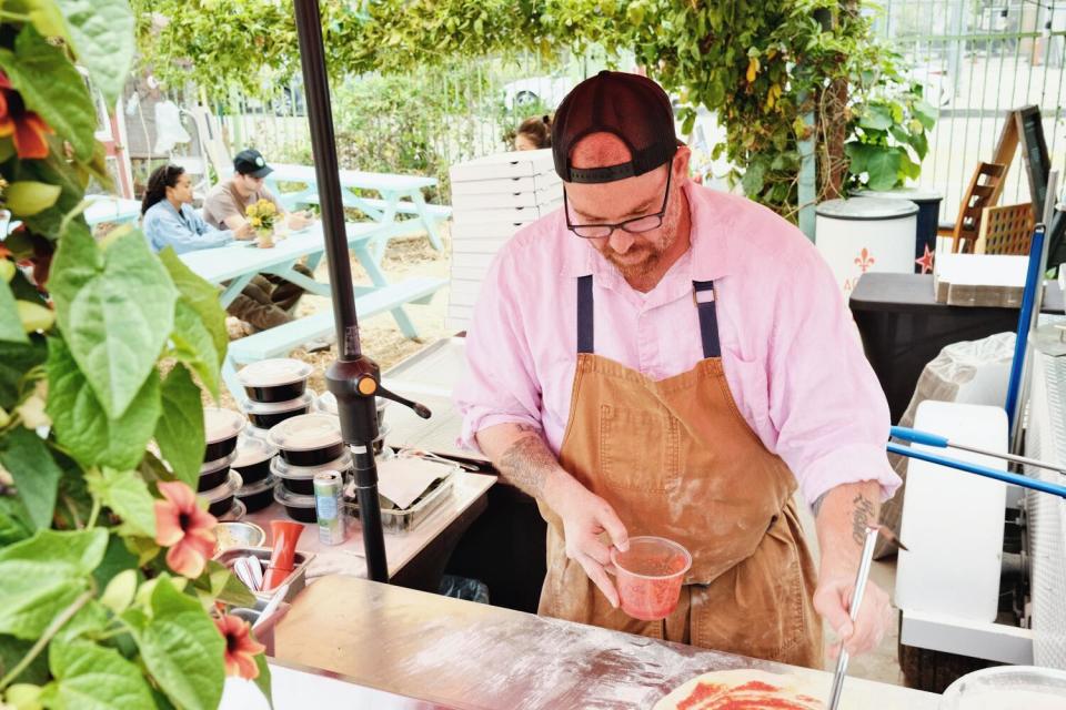 Michael Fiorelli ladles red sauce onto pizza dough at the outdoor Fiorelli Pizza. Guests at picnic tables in the background.