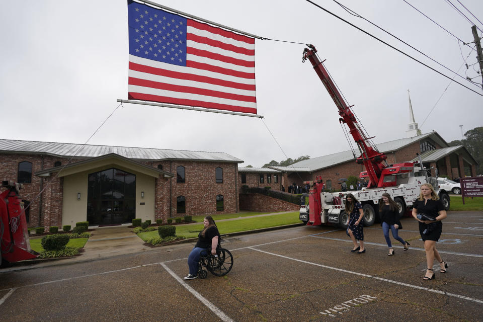 Attendees of the funeral services for Louisiana State Police Master Trooper Chris Hollingsworth, walk past a suspended American flag, Friday, Sept. 25, 2020, in West Monroe, La. Hollingsworth, killed in a car crash hours after he was told he would be fired for his role in the death of a Black man, was buried with honors Friday at a ceremony that authorities sought to keep secret out of concerns it would attract a mass protest. (AP Photo/Rogelio V. Solis)