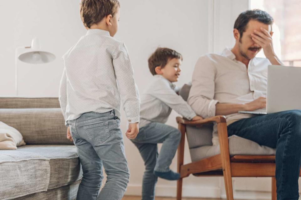 <p>Getty</p> Father frazzled on computer with two young sons