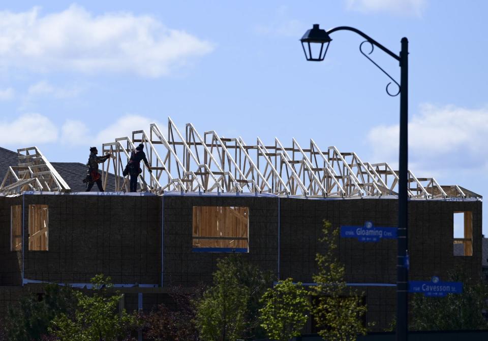 Two construction workers work on the roof of a house being built