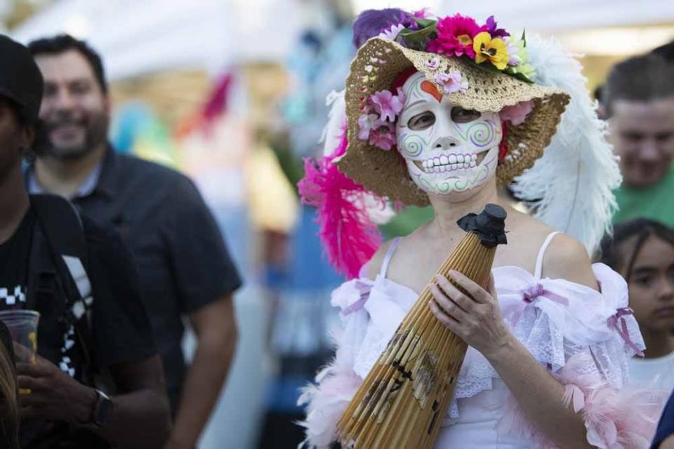 A woman dressed in traditional Dia De Los Muertos attire walking around and taking pictures with people at the Dia De Los Muertos Festival at Steele Indian School Park on Oct. 30, 2022, in Phoenix.