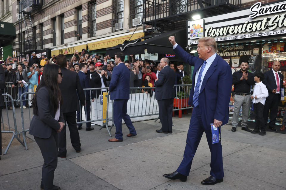 Former president Donald Trump, motions to a crowd after visiting a bodega, Tuesday, April 16, 2024, who's owner was attacked last year in New York. Fresh from a Manhattan courtroom, Donald Trump visited a New York bodega where a man was stabbed to death, a stark pivot for the former president as he juggles being a criminal defendant and the Republican challenger intent on blaming President Joe Biden for crime. Alba's attorney, Rich Cardinale, second from left, and Fransisco Marte, president of the Bodega Association, looked on. (AP Photo/Yuki Iwamura)