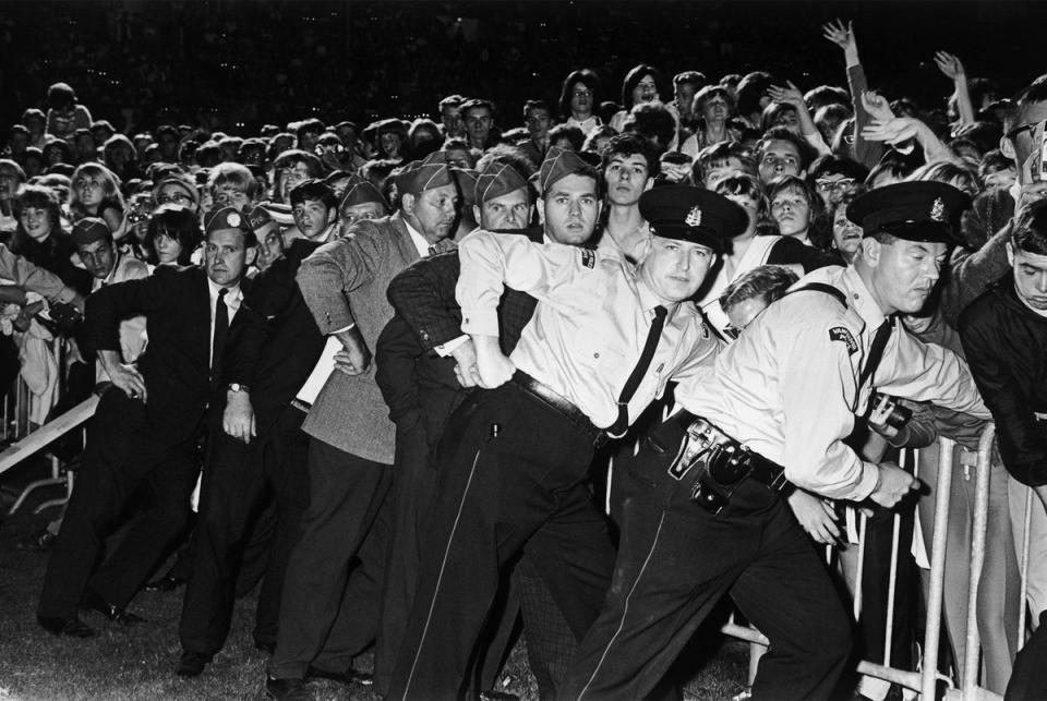 Police and security guards hold back Beatles fans at a concert in Vancouver during the group’s North American tour in 1964 (Getty)