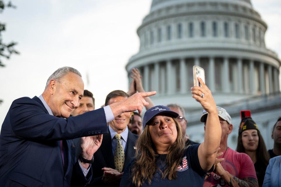 Senate Majority Leader Chuck Schumer points to the image on Rosie Torres's cell phone while she video calls her husband, veteran Le Roy Torres who suffers from illnesses related to his exposure to burn pits in Iraq, after the Senate passed the PACT Act at the U.S. Capitol August 2, 2022 in Washington, DC.