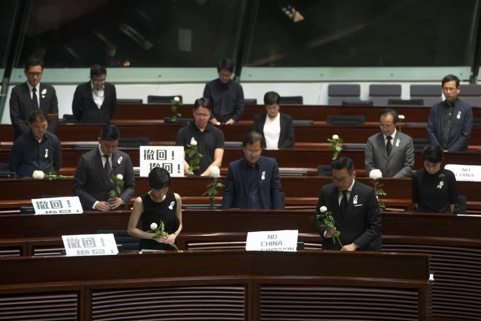 Pro-democracy lawmakers pay a silent tribute to the man who fell to his death on Saturday evening after hanging a protest banner on scaffolding on a shopping mall, at the Legislative Council in Hong Kong, Wednesday, June 19, 2019. Hong Kong lawmakers are meeting for the first time in a week, after massive protests over an extradition bill that eventually was suspended. The placards with Chinese read "Withdraw". (AP Photo/Kin Cheung)