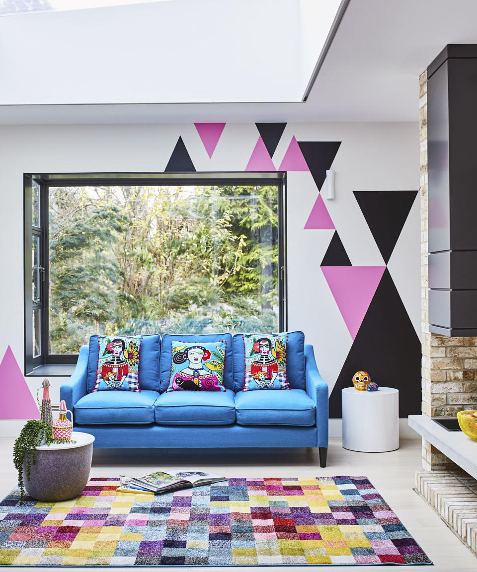 <p> Not into a full-on feature wall? You don&apos;t have to be. Contrary to popular opinion, a feature wall doesn&apos;t have to be as overwhelming as you might think. This playful pink and black triangular motif spans a mere third of the wall to add a fun twist to a white wall. </p> <p> We love the way it&apos;s been paired with the rectangular living room rug which is decorated with multicolored squares for a kaleidoscopic lounge aesthetic! </p>