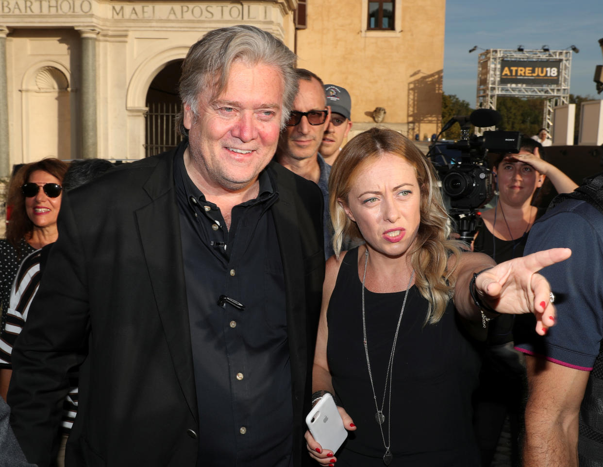 Steve Bannon and Giorgia Meloni stand together outside in artificial light near cameras.