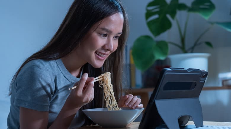 Woman eating noodles watching video