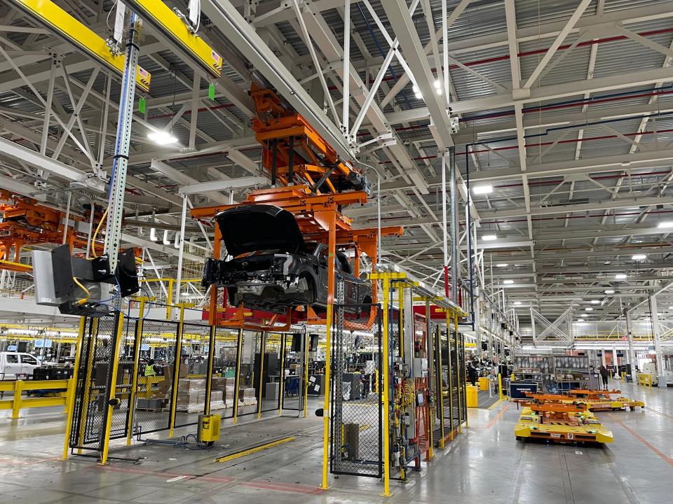 A partially built F-150 Lightning is suspended next to some of the automated pallets that move the vehicle around the factory.