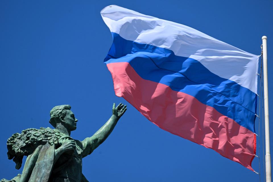 This photograph taken on on June 12, 2023 shows the Russian national flag next to a sculpture at the All-Russia Exhibition Centre (VDNKh), a trade show and amusement park in Moscow during the Russia Day celebration.