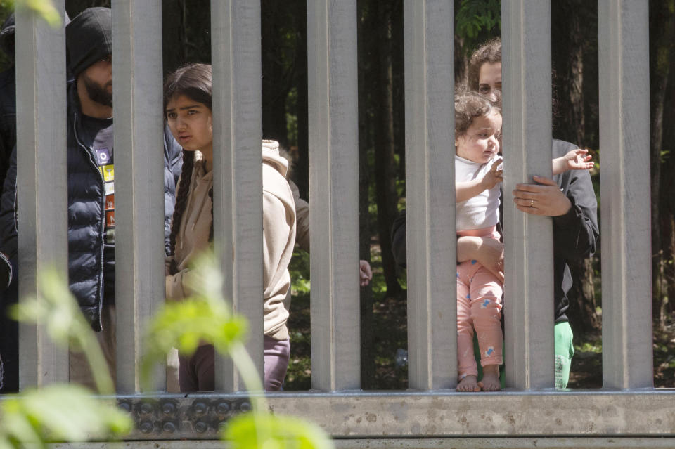 Members of a group of some 30 migrants seeking asylum are seen in Bialowieza, Poland, on Sunday, 28 May 2023 across a wall that Poland has built on its border with Belarus to stop massive migrant pressure. The group has remained stuck at the spot for three days, according to human rights activists. (AP Photo/Agnieszka Sadowska)