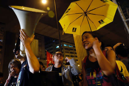 A protester holds a yellow umbrella, the symbol of the Occupy Central movement, in support of jailed Hong Kong student leaders Joshua Wong, Nathan Law and Alex Chow, while officers from the Correctional Services Department stand guard outside a prison in Hong Kong, China August 18, 2017. REUTERS/Tyrone Siu