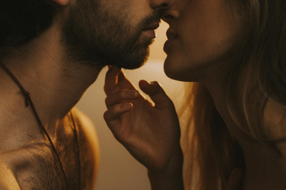 A close-up of a man with a beard and a woman, faces near each other, about to kiss intimately, with a romantic and passionate ambiance