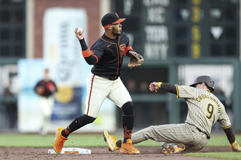 San Francisco Giants' Thairo Estrada, left, throws to first base after forcing San Diego Padres' Jake Cronenworth (9) out at second base on a double play hit into by Manny Machado during the third inning of a baseball game in San Francisco, Saturday, April 6, 2024. (AP Photo/Kavin Mistry)