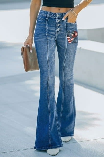 Person standing in flared jeans with a star-spangled pocket detail, carrying a brown clutch