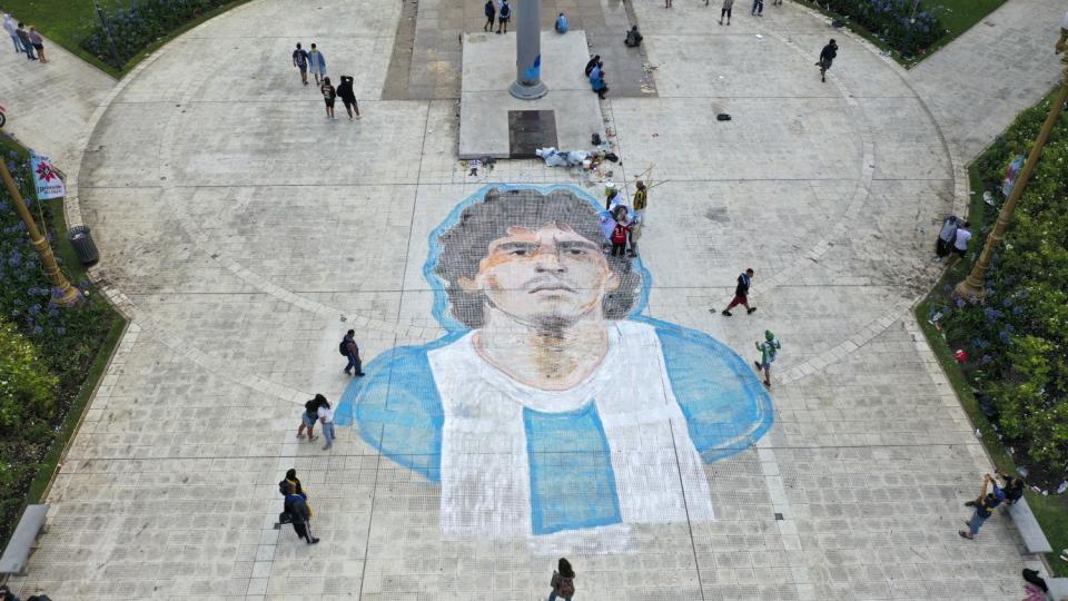 People walk past mural of Diego Maradona painted on the Plaza de Mayo in front of the presidential palace in Buenos Aires.