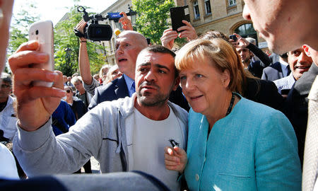 FILE PHOTO: A migrant takes a selfie with German Chancellor Angela Merkel outside a refugee camp near the Federal Office for Migration and Refugees after registration at Berlin's Spandau district, Germany September 10, 2015. REUTERS/Fabrizio Bensch/File Photo