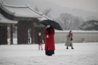 An employee wearing a face mask as a precaution against the coronavirus uses an umbrella to take shelter from the snow at the Gyeongbok Palace, one of South Korea's well-known landmarks, in Seoul, South Korea, Sunday, Dec. 13, 2020. (AP Photo/Lee Jin-man)