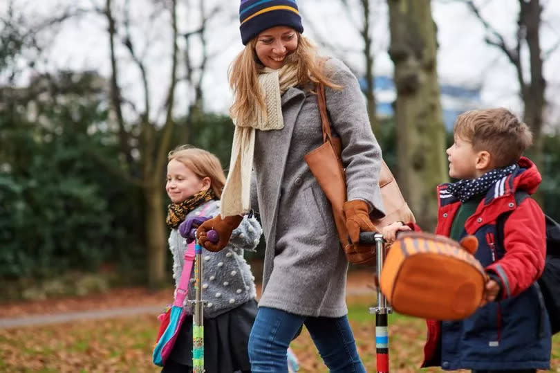 Young mum walking her children from school with their scooters, on cold autumn afternoon