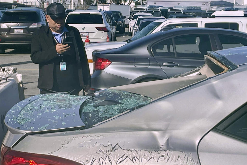 A man views damaged cars in an on-airport employee parking lot after tire debris from a Boeing 777 landed on them at San Francisco International Airport, Thursday, March 7, 2024. A United Airlines jetliner bound for Japan made a safe landing in Los Angeles on Thursday after losing a tire while taking off from San Francisco. (AP Photo/Haven Daley)