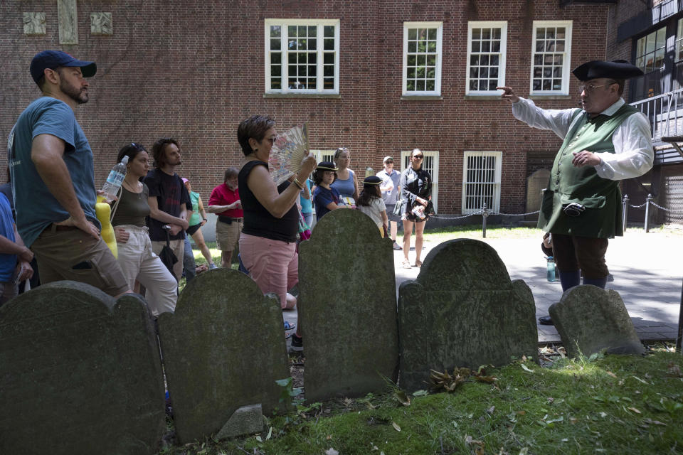 A guide dressed in a Colonial Era costume conducts a tour in the Granary Burying Ground on the Freedom Trail, Friday, June 17, 2022, in Boston. The summer of 2022 can feel as if the coronavirus pandemic is really over. Mask rules and testing requirements are lifting in many countries, including the United States. (AP Photo/Michael Dwyer)