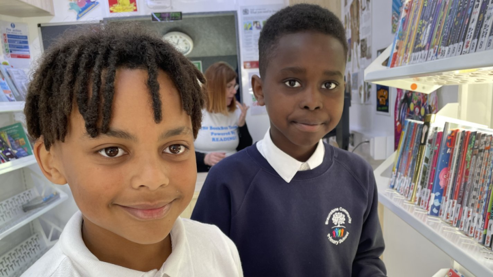 two boys stand inside the bus next to shelves of books smiling 