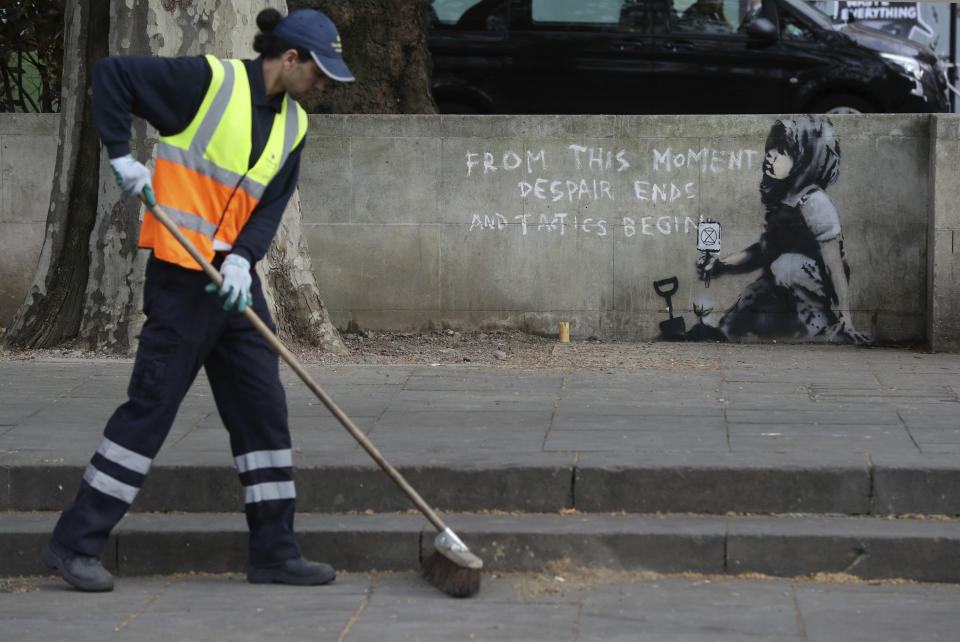 A road worker passes by an artwork which appears to be by street artist Banksy which has appeared near the former location of the Extinction Rebellion camp in Marble Arch, London, Friday April 26, 2019. (Jonathan Brady/PA via AP)