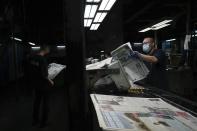 Workers check the copies of Apple Daily newspaper at the printing house in Hong Kong, early Friday, June 18, 2021. Five editors and executives at pro-democracy Apple Daily newspaper were arrested Thursday under Hong Kong's national security law, its stock was halted and police were searching its offices in moves raising concerns about the media's future in the city. (AP Photo/Kin Cheung)