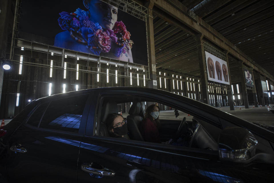 People take in an art exhibit from their car as they drive through a warehouse displaying paintings and photos in Sao Paulo, Brazil, Friday, July 24, 2020, amid the new coronavirus pandemic. Galleries, cinemas, theaters and museums are closed due to the restrictive measures to avoid the spread of COVID-19, but a group of artists and a curator found a way to overcome the restrictions to share their art with the residents of Brazil’s largest city. (AP Photo/Andre Penner)