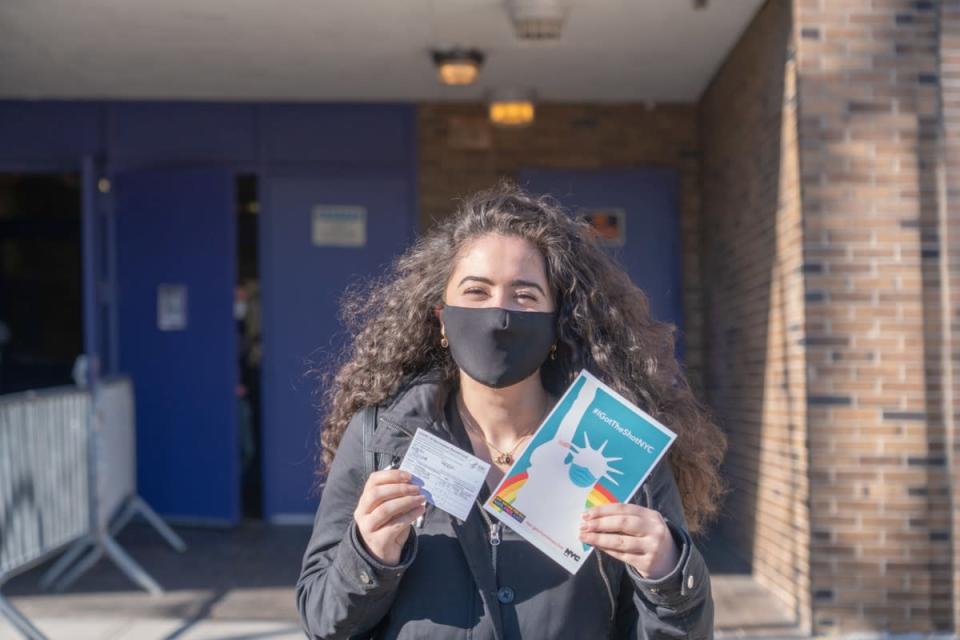 A woman displays her vaccination card and the “IGotTheShotNYC” banner after exiting the NYC Health Department Vaccine Hub at Hillcrest High School in Queens