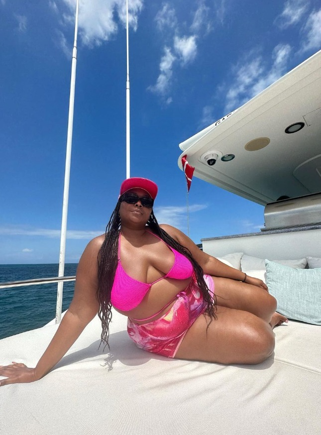 lizzo poses on a boat in a bright pink bikini