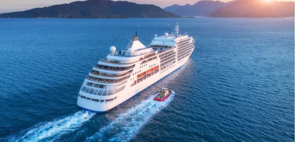 Cruise ship at harbor. Aerial view of beautiful large white ship at sunset. Colorful landscape with boats in marina bay, sea, colorful sky. Top view from drone of yacht. Luxury cruise. Floating liner