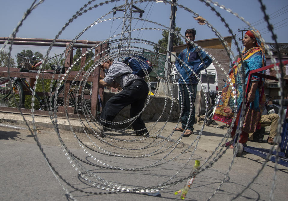 CORRECTS AGE - Kashmiri civilians cross a barricade set up by the police in Srinagar, Indian controlled Kashmir, Thursday, Sept. 2, 2021. Indian authorities cracked down on public movement and imposed a near-total communications blackout Thursday in disputed Kashmir after the death of Syed Ali Geelani, a top separatist leader who became the emblem of the region’s defiance against New Delhi. Geelani, who died late Wednesday at age 91, was buried in a quiet funeral organized by authorities under harsh restrictions, his son Naseem Geelani told The Associated Press. He said the family had planned the burial at the main martyrs’ graveyard in Srinagar, the region’s main city, as per his will but were disallowed by police. (AP Photo/ Mukhtar Khan)