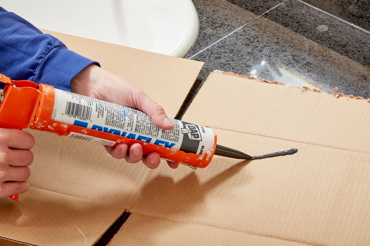 A person learning how to use a caulk gun before applying new caulking around a shower and bathtub.