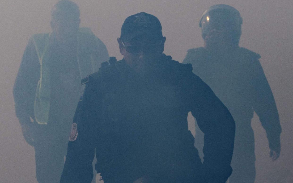 Mexico's Federal Police officers are seen through the smoke of tear gas thrown by the US Border Patrol to disperse Central American migrants - AFP