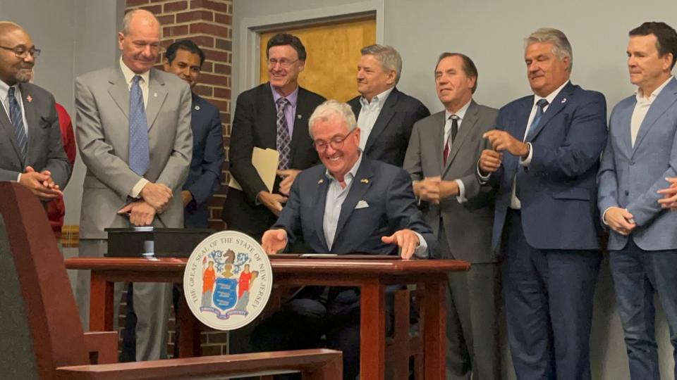 New Jersey Gov. Phil Murphy signs a document to start the review process on an amendment that will allow for a film and television campus at Fort Monmouth. Standing to his left with hands crossed is Greg Hanco, president of local chapter 59 of the International Alliance of Theatrical Stage Employees union. Directly behind him is Netflix co-CEO Ted Sarandos. To Sarandos' right is New Jersey state Assembly Speaker Craig Coughlin, and Monmouth and Ocean Counties President for the Building and Construction Trades Council Thomas DeBartolo.