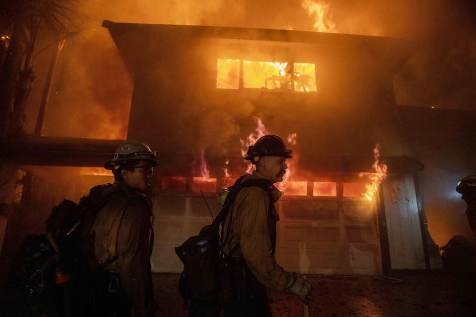 FILE - In this Oct. 31, 2019, file photo, firefighters work to prevent a house fire from spreading to other homes during the Hillside fire, in San Bernardino, Calif. The virus outbreak is compromising the ability of nations to prepare for natural disasters and deal with the aftermath. Every year, the world contends with devastating typhoons, wildfires, tsunamis and earthquakes. (AP Photo/ Christian Monterrosa, File)