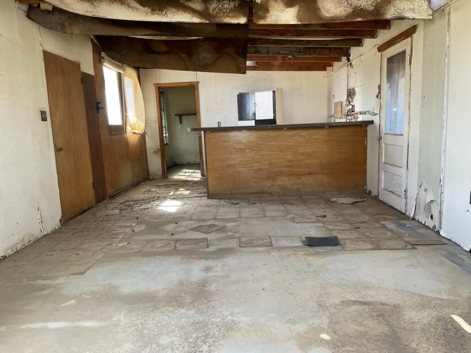 Interior of empty house with partly torn up floor tiles and deteriorating walls and ceiling.