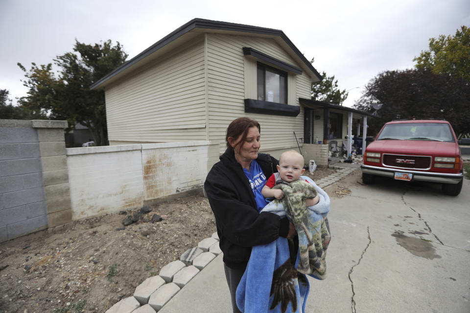 FILE - In this Oct. 9, 2019, file photo, Alanna Mabey holds her grandson in front of her home in West Valley City, Utah. Assessor Paul Petersen sold the house this spring as complaints mounted from neighbors in the working-class area in suburban Salt Lake City, said new owner Mabey. Authorities say Petersen used homes like this one to lodge pregnant women from the Marshall Islands who were offered money to come to the U.S. to give up their children for adoption. Petersen, the assessor of Arizona's most populous county, was charged in Utah, Arizona and Arkansas with counts including human smuggling, sale of a child, fraud, forgery and conspiracy to commit money laundering. The Maricopa County Board of Supervisors voted unanimously Wednesday, Oct. 23, to notify Petersen that it plans to consider suspending him for up to 120 days. It can't remove him from office and he's refused to resign. (AP Photo/Rick Bowmer, File)