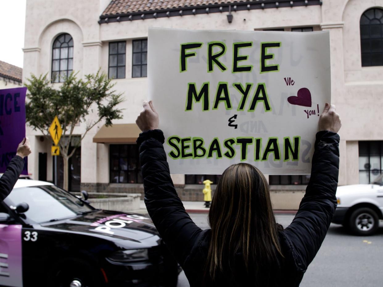 A woman holds a white poster reading "Free Maya and Sebastian."