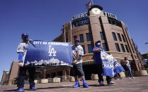 Los Angeles Dodgers fans Oliver Olson, left, of San Diego, Juan Campo and Rudy Soto, both of Los Angeles, hold up flags outside the main entrance to Coors Field as fans return for the first inning of a baseball game between the Dodgers and Colorado Rockies Thursday, April 1, 2021, in Denver. (AP Photo/David Zalubowski)