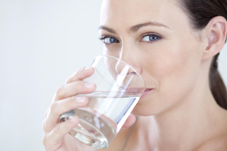 Frau mit schönem Teint trinkt ein Glas Wasser.