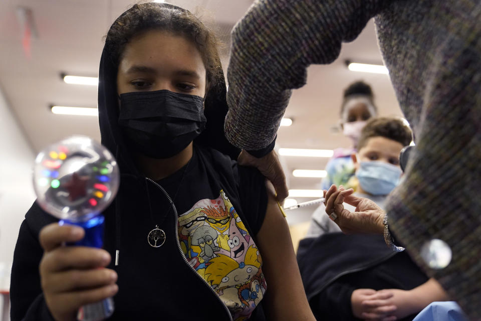 Nyell Conyer, 11, of Worcester, Mass., left, focuses on a spinning toy while receiving a shot of Pfizer COVID-19 vaccine, Thursday, Dec. 2, 2021, at a mobile vaccination clinic, in Worcester. As the U.S. recorded its first confirmed case of the omicron variant, doctors across the country are experiencing a more imminent crisis with a delta variant that is sending record numbers of people to the hospital in New England and the Midwest. (AP Photo/Steven Senne)