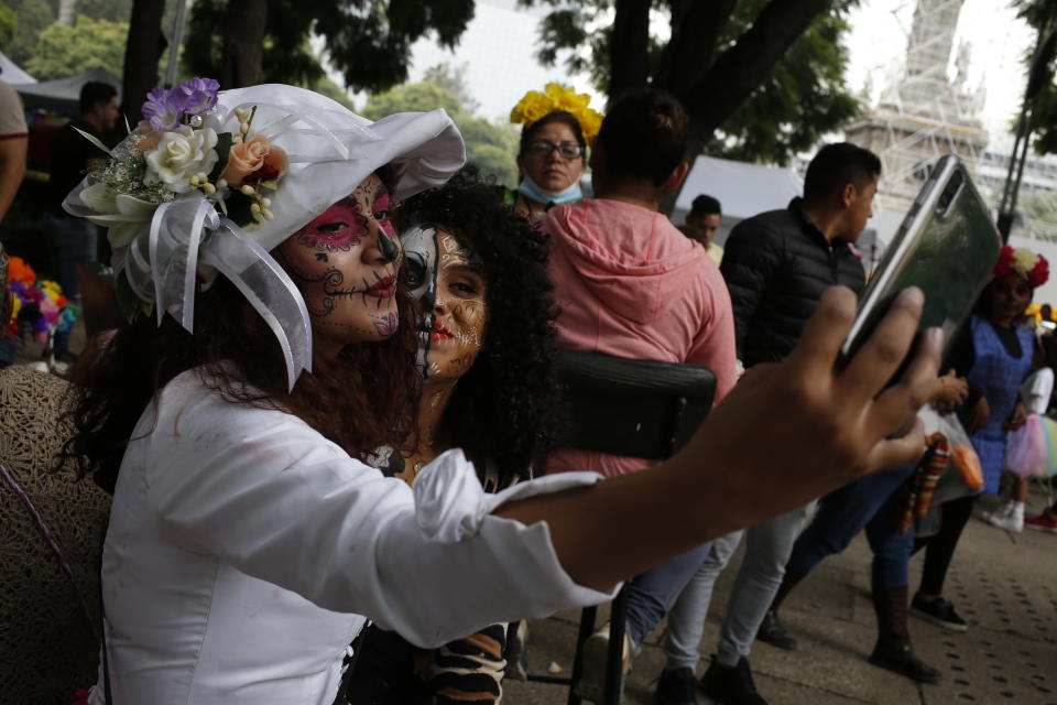 Women wearing Catrina makeup take a selfie before the parade down Mexico City's iconic Reforma avenue during celebrations for the Day of the Dead, Saturday, Oct. 26, 2019. (AP Photo/Ginnette Riquelme)